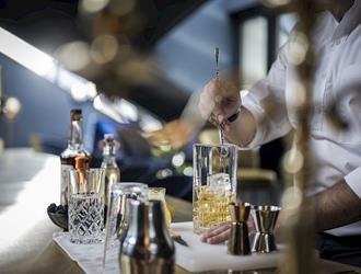 Ein Barkeeper, der einen Drink mit Eiswürfeln in einem Rührglas zubereitet