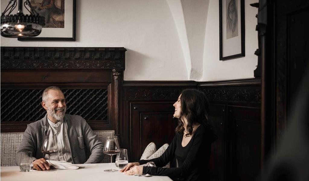 A man and a woman are sitting at a table, drinking a glass of red wine