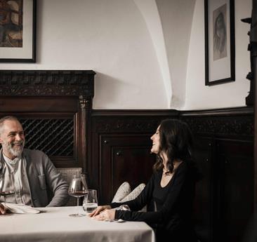 A man and a woman are sitting at a table, drinking a glass of red wine