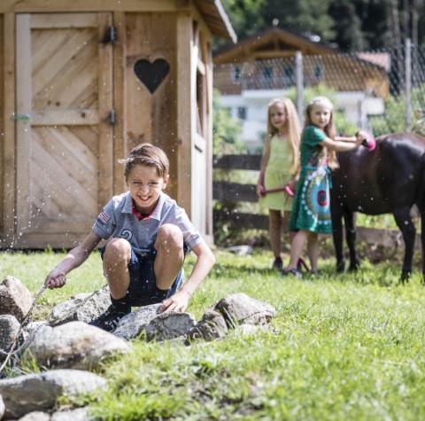 Two children are grooming a horse, and a boy is sitting by the pond