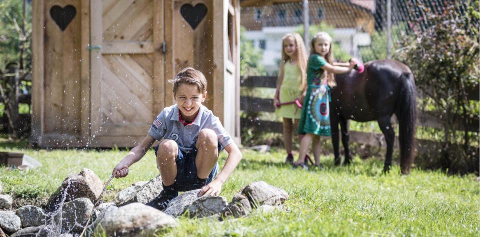 Due bambini strigliano un cavallo e un ragazzo è seduto vicino allo stagno
