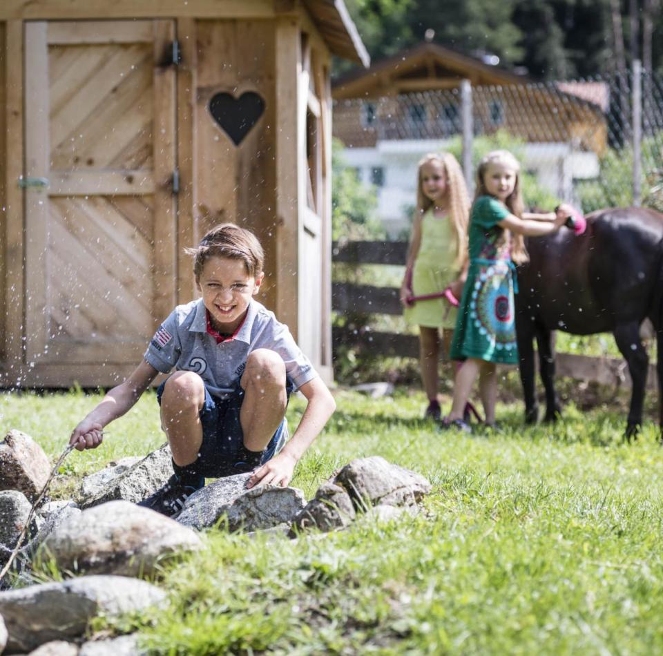 Due bambini strigliano un cavallo e un ragazzo è seduto vicino allo stagno