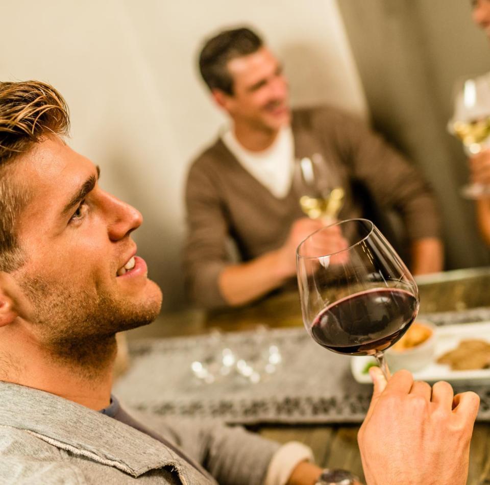 Two men and a woman are sitting at a table and drinking a glass of wine