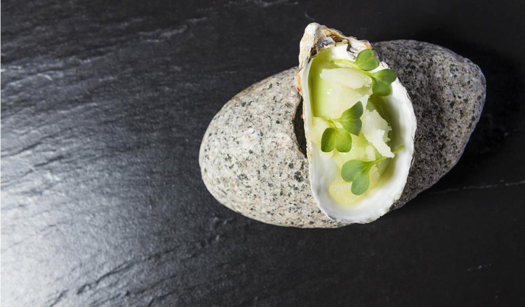 Ein kunstvoll angerichtetes Gericht in einer Muschelschale, serviert auf einem Steinuntergrund