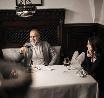 A man and a woman are sitting at a table, drinking a glass of red wine