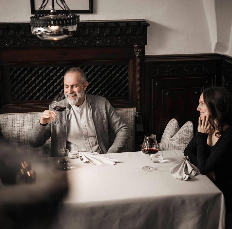 Ein Mann und eine Frau sitzen an einem Tisch und trinken ein Glas Rotwein