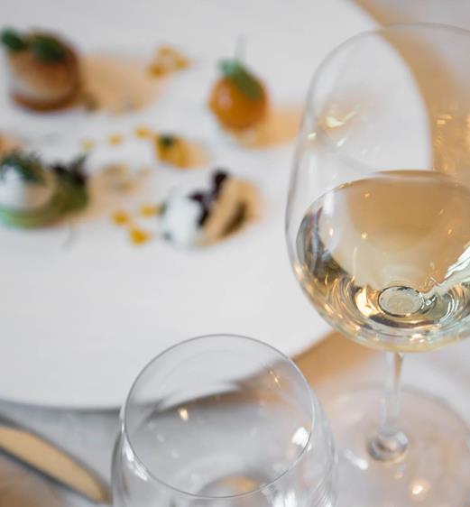 Un bicchiere di vino bianco e, sullo sfondo, un piatto