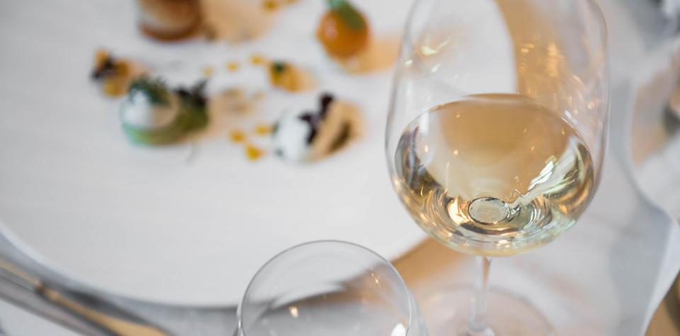 Un bicchiere di vino bianco e, sullo sfondo, un piatto