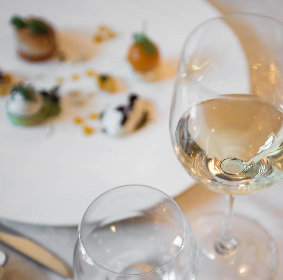 A glass of white wine with a dish in the background