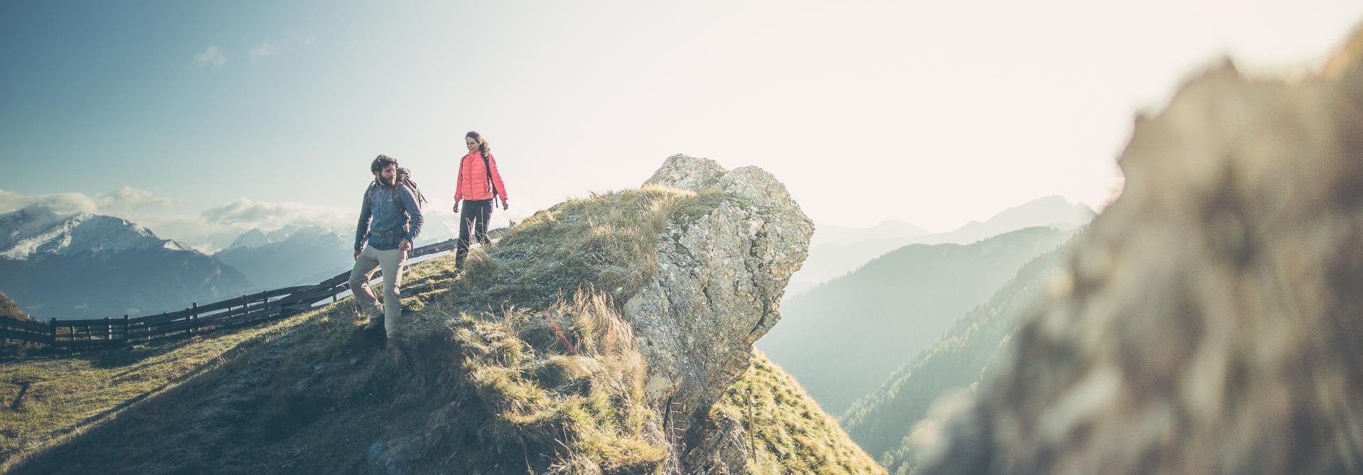 Zwei Wanderer stehen auf einem Berggrat und blicken über die Alpen