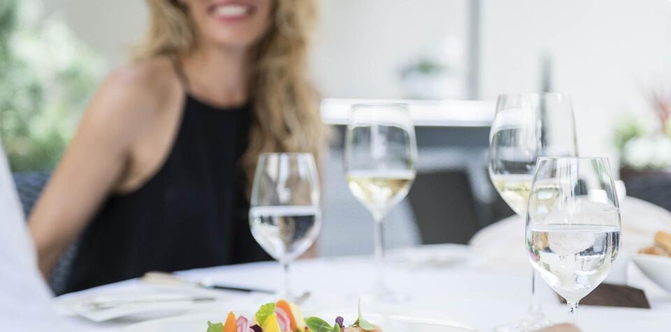 Eine Frau sitzt lächelnd an einem elegant gedeckten Tisch und genießt ein Glas Weißwein