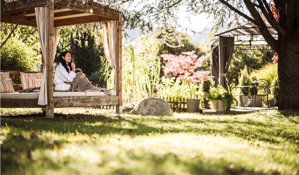 Eine Person entspannt im Gartenpavillon, umgeben von Sonne und Natur
