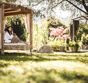 Eine Person entspannt im Gartenpavillon, umgeben von Sonne und Natur