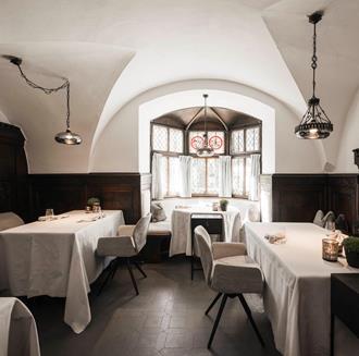 The Stube of Hotel Stafler shows a bright room with white-covered tables and traditional wooden furnishings