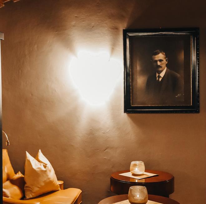 Un’accogliente area lounge con un divano in pelle, luce calda e un ritratto appeso alla parete