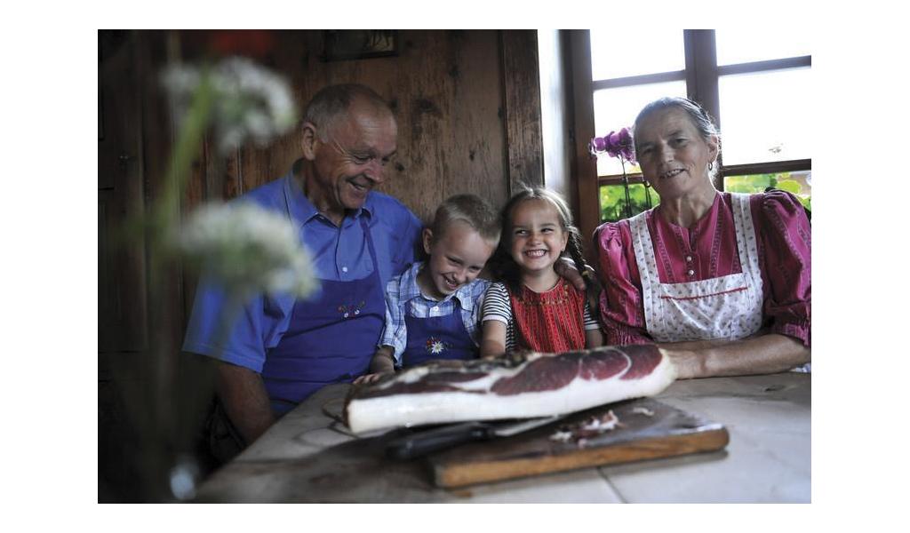 Eine Bauernfamilie in einer alten Stube, auf dem Tisch liegt ein großes Stück Speck