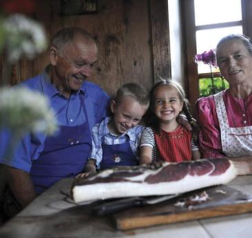 Una famiglia contadina in una vecchia stube, con un grande pezzo di speck sul tavolo