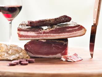 Auf einem Holzbrett befindet sich Speck, Kaminwurzen und Schüttelbrot