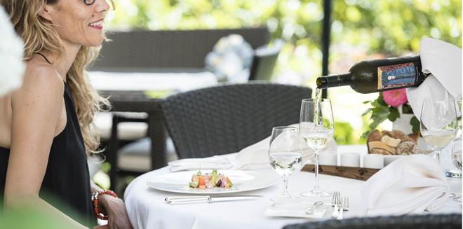 Eine Frau sitzt an einem gedeckten Tisch und bekommt ein Glas Wein eingeschenkt