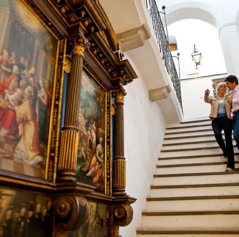 A woman and a man are standing on a staircase in a historic building