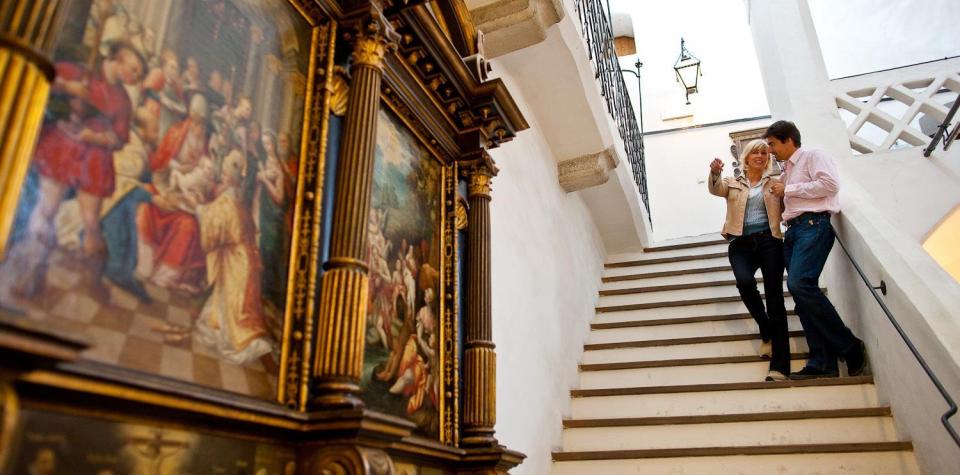A woman and a man are standing on a staircase in a historic building