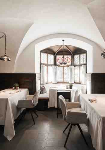 La Stube dell’Hotel Stafler mostra un ambiente luminoso con tavoli apparecchiati di bianco e un arredamento tradizionale in legno