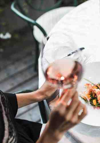 Eine Frau sitzt an einem Tisch mit einem Glas Roséwein und einem zubereiteten Gericht